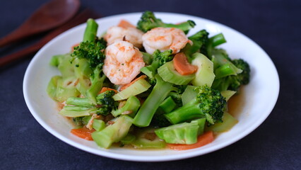 table top view stir-fried broccoli with shrimp and carrot in white plate isolated on black background.