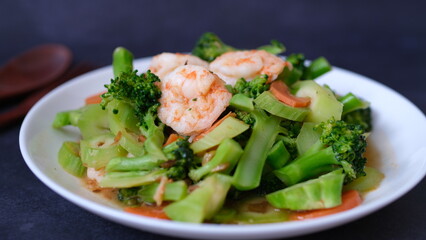 table top view stir-fried broccoli with shrimp and carrot in white plate isolated on black background.