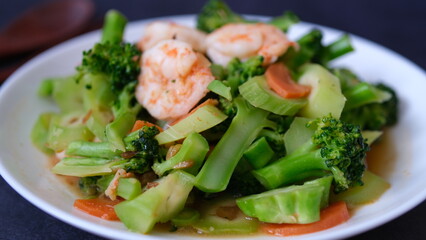 table top view stir-fried broccoli with shrimp and carrot in white plate isolated on black background.