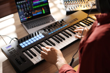 Man working with MIDI keyboard at wooden table indoors, above view