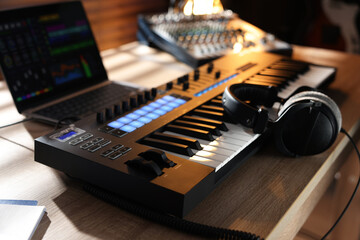 MIDI keyboard with headphones, laptop and dj mixer on wooden table indoors, closeup
