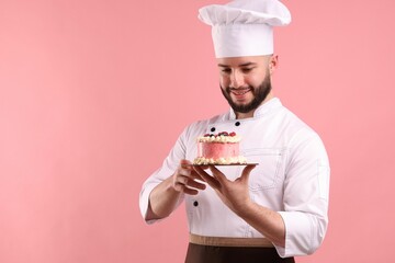 Happy confectioner in uniform holding cake with berries on pink background
