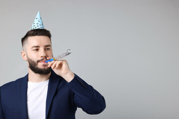 Happy Birthday. Handsome man with party hat and blower on grey background, space for text