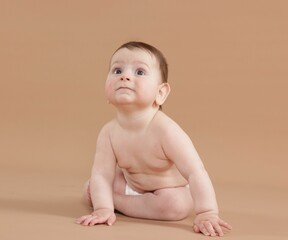 Cute little baby in diaper sitting on beige background