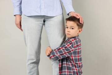 Little boy afraid to leave without mother and hugging her on grey background. Separation anxiety
