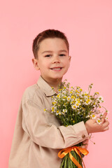 Portrait of smiling little boy with bouquet of beautiful chamomile flowers on pink background