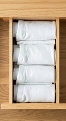 A top view of a light wood drawer filled with neatly folded white towels stacked on each other