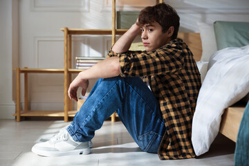Teen problems. Depressed teenage boy near bed at home