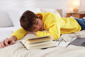 Tired teenage student sleeping near books and laptop on bed at home