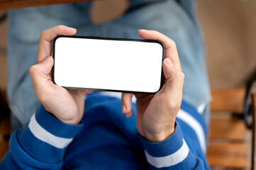 Close up of hands holding smartphone horizontally while sitting at wooden table in cafe or canteen.