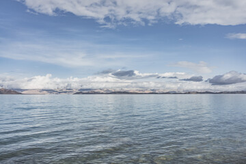 Panorama landscape of Lake Karakul in the Pamir mountains in the Tien Shan against the background of high snowy rocky peaks with clouds, morning panorama of the lake for the background
