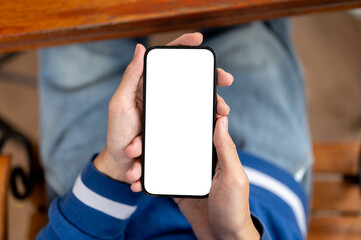 Close up of a man holding smartphone with both hand while sitting at wooden table in cafe or canteen