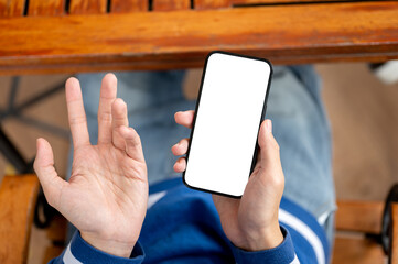 Close up of hands holding smartphone with open palm while sitting at wooden table in cafe or canteen