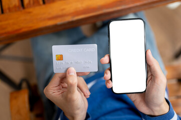 Close up of a man holding or looking at phone and credit card at wooden table in a cafe or canteen.