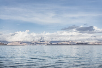 Panorama landscape of Lake Karakul in the Pamir mountains in the Tien Shan against the background of high snowy rocky peaks with clouds, morning panorama of the lake for the background