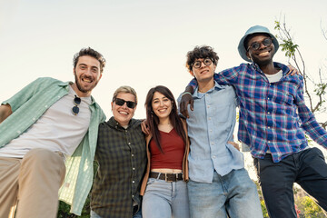 Low angle portrait of a happy multiethnic group of young friends. Concept of friendship, diversity, community and youth lifestyle. A cheerful team smiling together at camera outdoors.