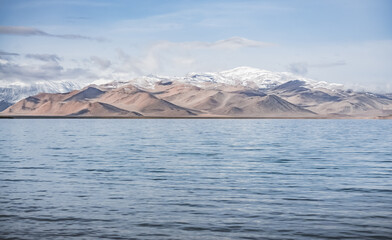 Panorama landscape of Lake Karakul in the Pamir mountains in the Tien Shan against the background of high snowy rocky peaks with clouds, morning panorama of the lake for the background