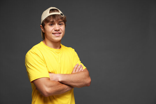 Portrait of smiling teenage boy in baseball hat with crossed arms on grey background. Space for text