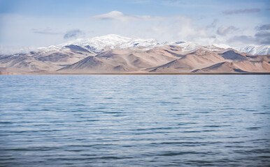 Panorama landscape of Lake Karakul in the Pamir mountains in the Tien Shan against the background of high snowy rocky peaks with clouds, morning panorama of the lake for the background