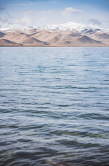 Panorama landscape of Lake Karakul in the Pamir mountains in the Tien Shan against the background of high snowy rocky peaks with clouds, morning panorama of the lake for the background