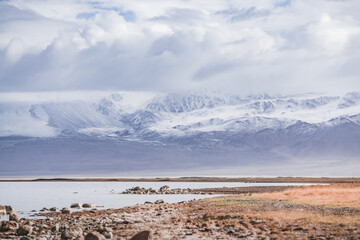 Rocky shore of Lake Karakul and blue water of a high mountain lake against the background of rocky mountain slopes in the Pamirs in the Tien Shan, panoramic landscape for background