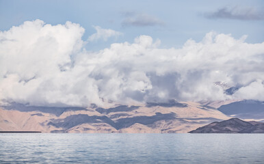 Panorama landscape of Lake Karakul in the Pamir mountains in the Tien Shan against the background of high snowy rocky peaks with clouds, morning panorama of the lake for the background