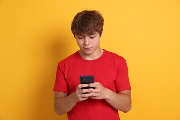 Fototapeta premium Teenage boy using smartphone on yellow background