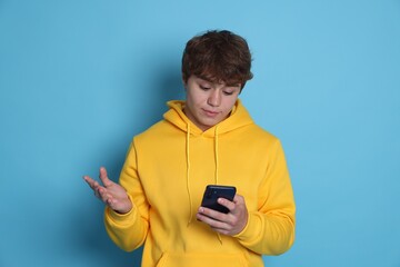 Teenage boy with smartphone on light blue background