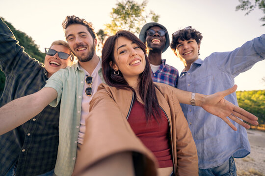 A happy young woman taking a selfie with her diverse friends outdoors. Point of view shot showing a multiethnic group celebrating friendship, community and togetherness.
