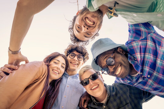 Low angle view of a happy diverse group of friends looking down at camera in a circle. Concept of community, teamwork, togetherness and friendship. Young multiethnic people having fun.