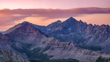 Aerial view of a mountain range under a colorful sky at dusk with visible rock formations and snow patches