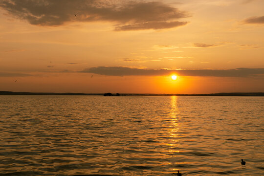 Golden sunset over calm water with reflections and gentle waves
