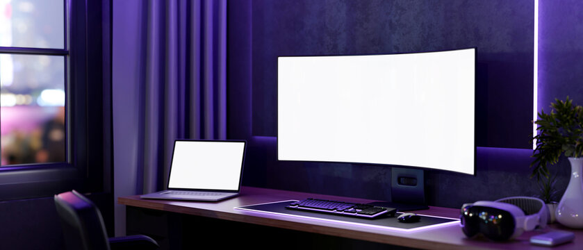 White screen computer and laptop with headset on wooden table with neon purple monitor backlighting.