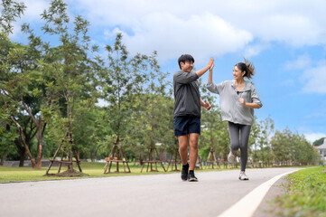 Asian woman in sportswear clapping or high five with a man during a run or jogging on pavement in...