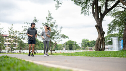 Obraz premium Asian woman and man in sportswear smiling and talking while running or jogging on pavement in park.