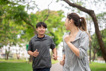 Obraz premium Asian woman and a man in sportswear talking together while exercising by running on pavement in park
