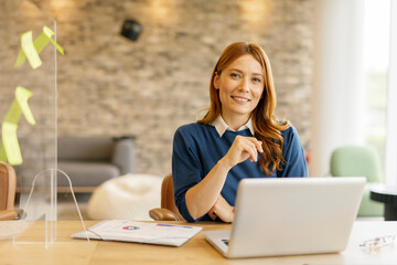Businesswoman smiling while working on a laptop in a modern office setting