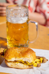 Traditional combination of food and drink in any German festivities, beer in a beer stein and sausage with bread and mustard on a outdoors table.