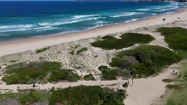 Sydney, Australia - UHD Video- Aerial View at Wanda Beach in Cronulla with silhouetted surfers walking the sand path to the beach on a beautiful summer day.