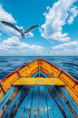 Colorful Wooden Boat on Open Sea with Seagulls. Front view of a vibrant blue and yellow wooden boat sailing on the open sea with seagulls flying under a bright blue sky.