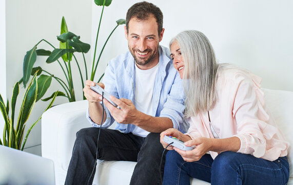 Happy man with mother playing video game sitting on sofa in living room at home