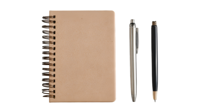 A tan notebook with a black spiral binding and two pens on a black background in a studio setting