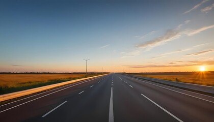Naklejka premium Empty highway stretching towards a vibrant sunset over golden fields