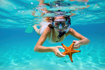 Naklejka premium Tourist snorkeling underwater is holding starfish in turquoise ocean