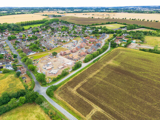 Aerial view of a large, new housing development featuring large, executive and smaller affordable homes seen next to an established village in rural England.