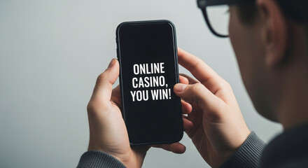 Smartphone in hands, the inscription "ONLINE CASINO, YOU WIN" on the smartphone screen, minimalism. Concept of gambling addiction, online fraud, fake casino.