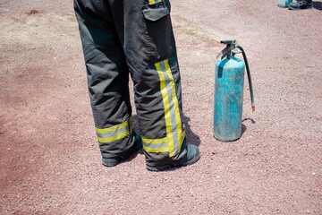 Imagen horizontal de los pies de un bombero con un extintor alado en la tierra