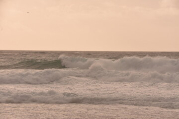 Powerful ocean waves crashing under a soft pastel-toned sky during sunset. The golden light of the...