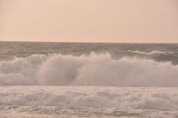 Powerful ocean waves crashing under a soft pastel-toned sky during sunset. The golden light of the...