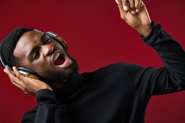Young African man singing passionately with headphones on a red background, expressing joy and...